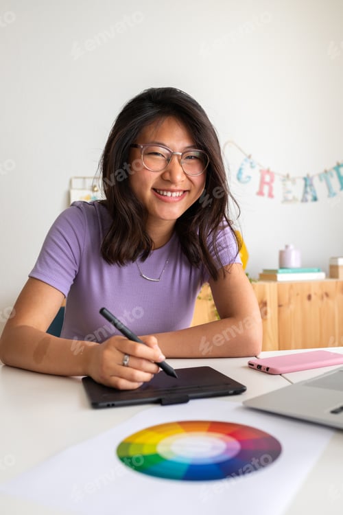 Preview: Asian female graphic design student working using tablet and laptop looking at camera.Vertical