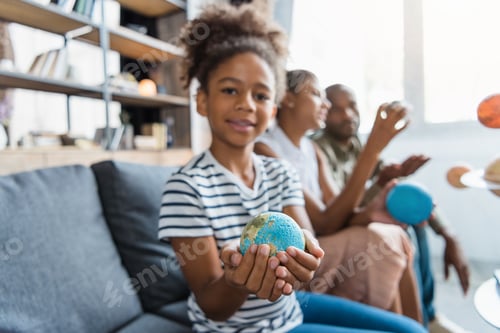 Preview: Little girl on a couch with a globe figurine in her hands, while her parents are sitting in the