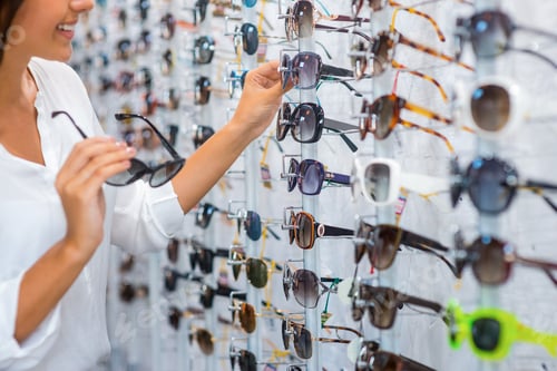 Preview: Choosing sunglasses in store. Close-up of cheerful young woman choosing sunglasses in store