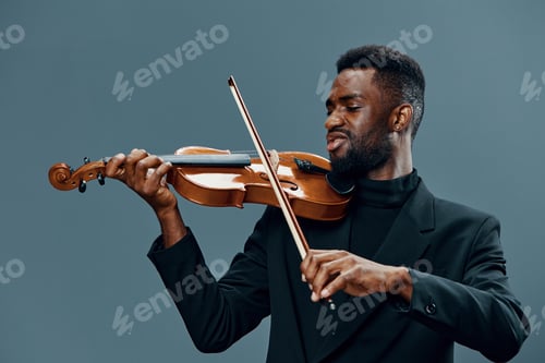 Preview: Talented African American man playing violin with passion and skill on gray background in studio