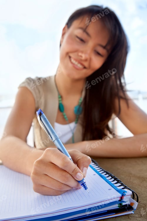 Preview: Female Student Writing On A Notebook And Smiling