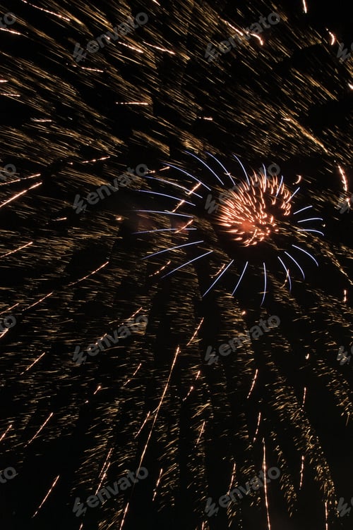 Preview: Fiery Burst Of Fireworks With Blue Streamers Amid Embers From Larger Previous Explosion