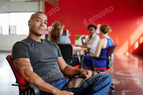 Preview: Confident Male Designer Working On A Digital Tablet In Red Creative Office Space