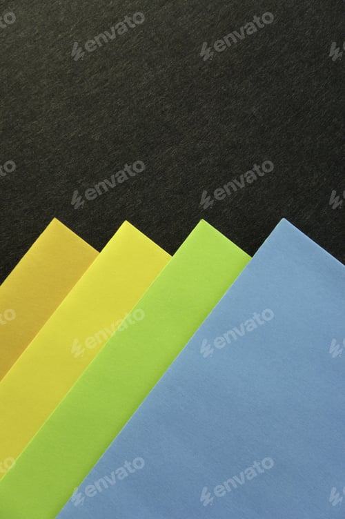 Preview: Corners Of Orange, Yellow, Green, And Blue Envelopes Aligned On Black Cardboard