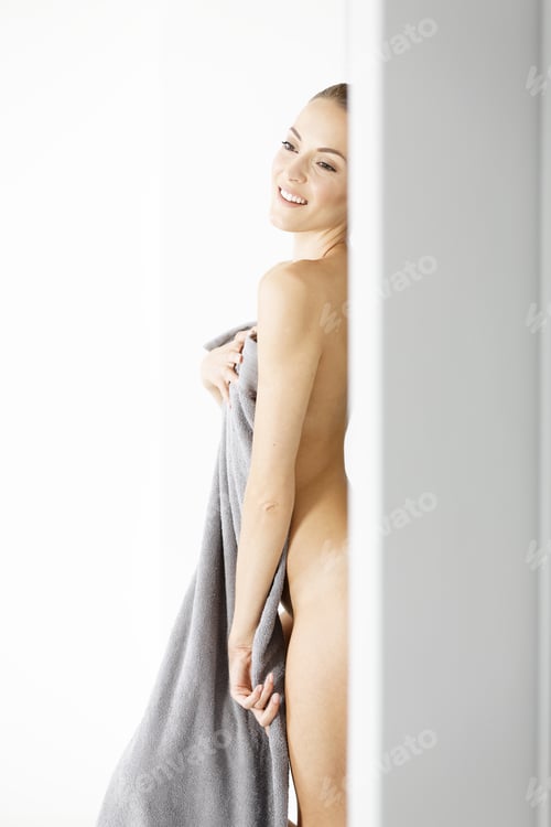 Preview: Attractive Naked Woman Leaning Against A Wall With A Towel Draped Over Her Getting Dressed