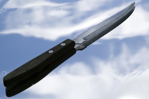 Preview: Serrated Knife And Its Shadow Against Blue Sky With Wispy Clouds