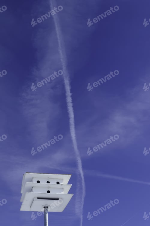 Preview: Flight Dreams: Jet Contrails In Blue Sky Above Top Of White Birdhouse