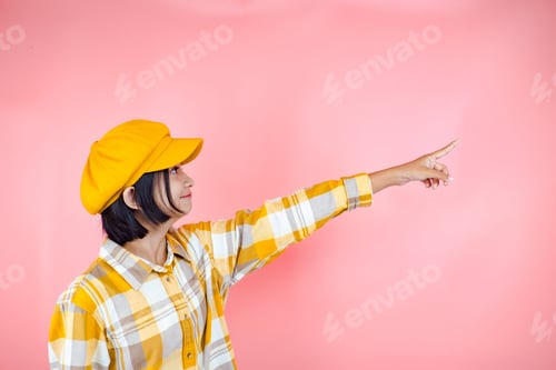 Preview: Happy Asia Young Girl Wear Yellow Shirt And Yellow Hat Point Up With Pink Background.
