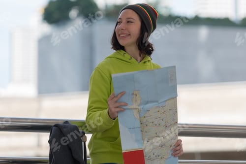 Preview: Happy Female Tourist With Suitcase Exploring Map While Standing In City Building