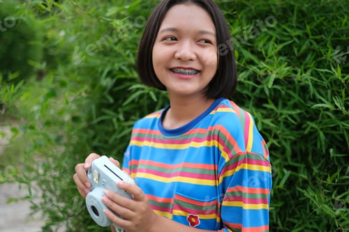 Preview: Happy Young Asian Girl With Blue Camera And Nature Background.