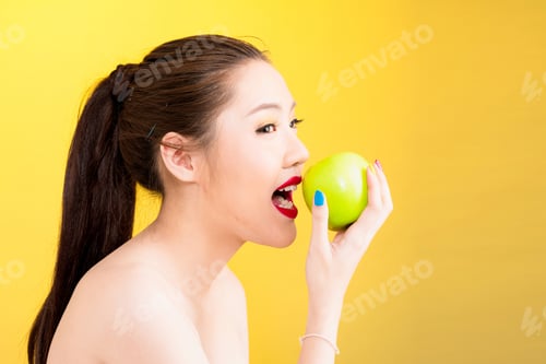 Preview: Young Asian Woman Biting Apple Isolated In Yellow Background. Portrait Of Beautiful Half Naked