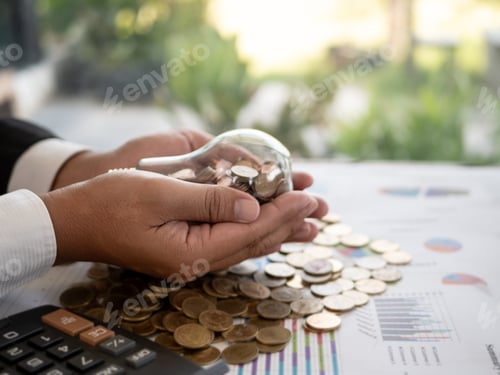 Preview: Hands Of Businessman Holding A Light Bulb With Coin. The Idea Of Reducing Costs And Reduce Energy