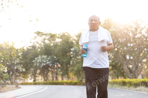 Preview: Front View Asian Elderly Exercise. Senior Man Holding Water Bottle Running On Road In Public Park