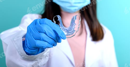 Preview: Dentist Woman Holding Orthodontic Retainer On Blue Screen Background. Dental Care And Healthy Teeth.