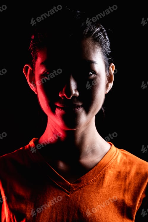 Preview: Portrait Of Woman In Dramatic Light. Asian Woman In Orange T-Shirt. Dark, Dramatic Lghting Set Up.