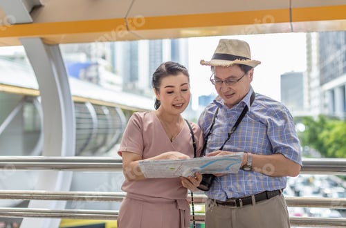 Preview: Senior Couple Traveling Together And Holding And Looking A Map, With Digital Camera, Bag And Hat On