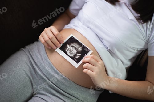 Preview: Pregnant Woman Keeping Hand On Belly And Holding Ultrasound Image At Home Interiors