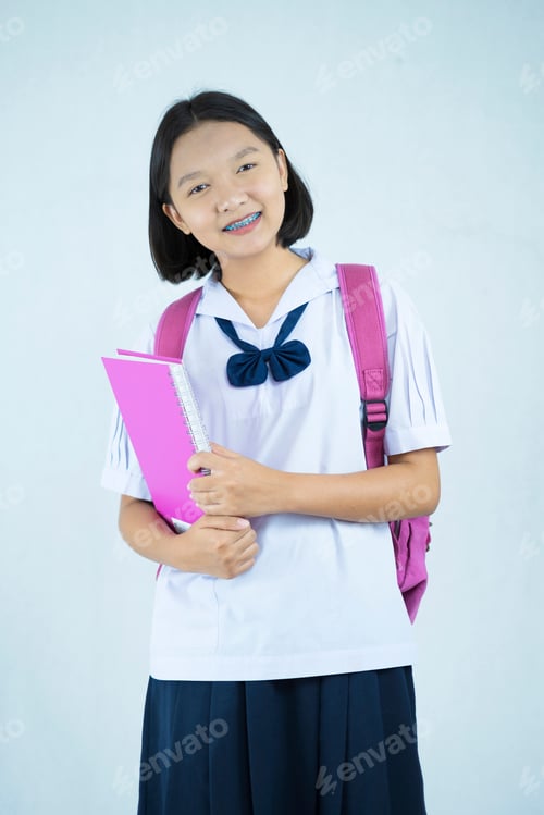 Visualização: Jovem asiática feliz em uniforme escolar segura livro rosa com fundo branco, estudante.