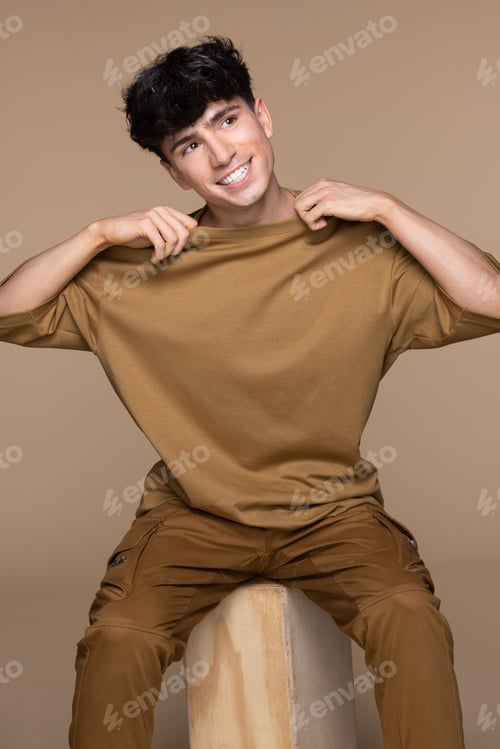 Preview: Studio Portrait Of Young Non-Binary Caucasian Man In His 20S Sitting On A Block Posing On Neutral