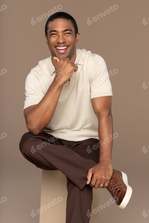 Preview: Studio Portrait Of Attractive Black Man In His 40S Sitting On A Box And Smiling On Neutral