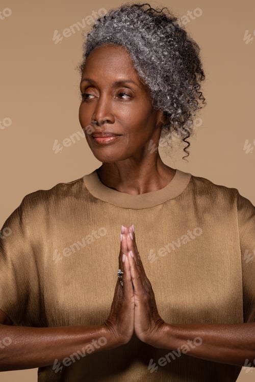 Preview: Portrait Of Beautiful Black Woman In Her Late 50S Posing With Her Hands Together Praying On Neutral