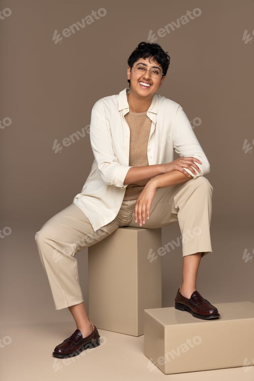 Preview: Full Length Shot Of Young Non-Binary Punjabi Person Smiling And Posing Confidently Sitting On Box