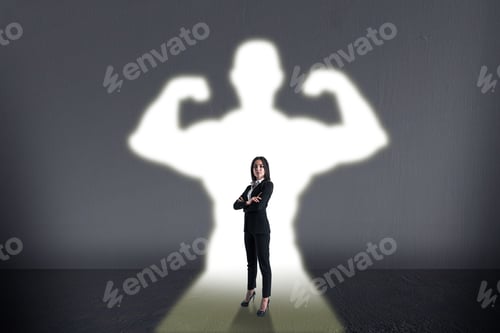 Preview: Attractive Young European Businesswoman With Creative White Muscle Arms Shadow On Concrete Wall