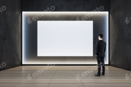 Preview: Businessman Standing In Modern Exhibition Hall Interior With Illuminated White Mock Up Wall And