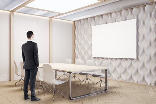Preview: Businessman Looking On Empty Poster In Conference Room. Workplace And Company Concept.