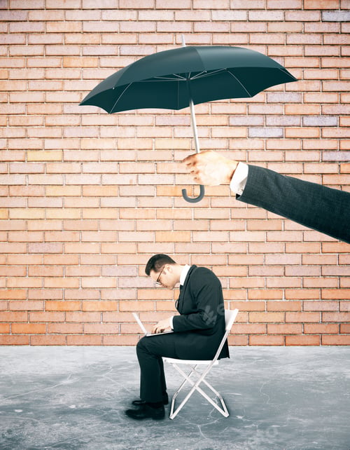 Preview: Hand Holding Umbrella Over Working Businessman. Protection Concept.Red Brick Wall Background