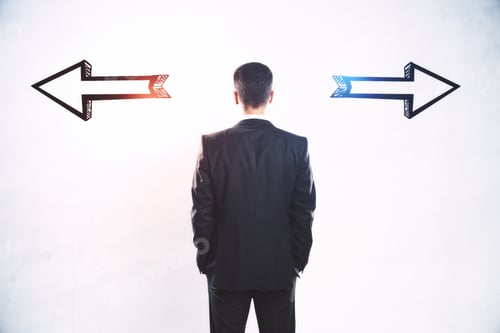 Preview: Businessman Standing Puzzled In Front Of A Wall With Two Black Silhouette Arrows Pointed In