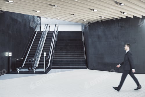 Preview: Businessman Walking In Train Station Interior With Escalator And Blank Copyspace On Concrete Wall