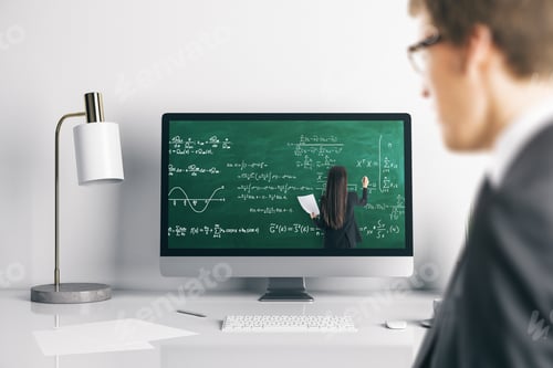 Preview: Young Businessman At Office Desk Looking At Computer Screen With Online Education Chalkboard And