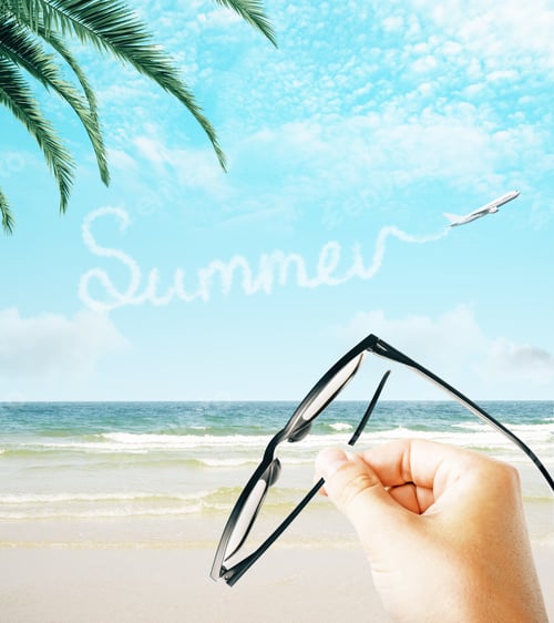 Preview: Hand Holding Eyeglasses On Creative Beach Background With Airplane And Text In Sky. Summer And
