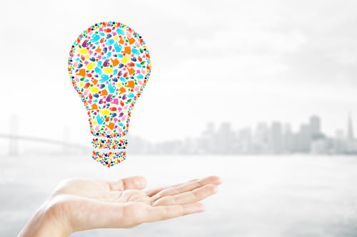 Preview: Held Creative Hand Gesture Lightbulb On Blurry City Background. Communication, Community, Inspire