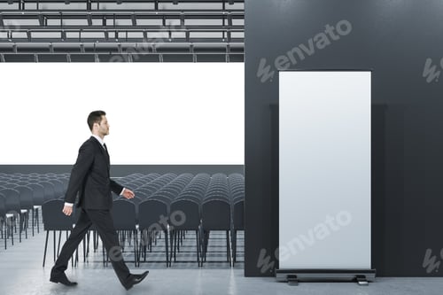 Preview: Businessman Standing In Modern Grey Auditorium With Seating, Empty Screen And Mock Up Poster For