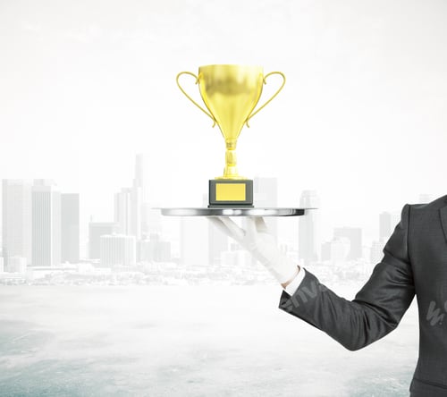 Preview: Businessman Hand In White Glove Holding Tray With Golden Cup Trophy On City Background