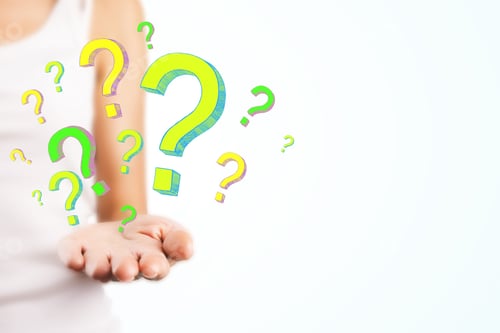 Preview: Blurry Female Hand Holding Drawn Question Marks On Subtle Background. Quiz And Confusion Concept