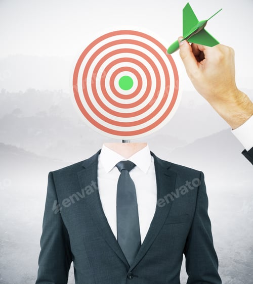 Preview: Hand With Green Dart Aiming At Target-Headed Businessman On Landscape Background. Aiming And