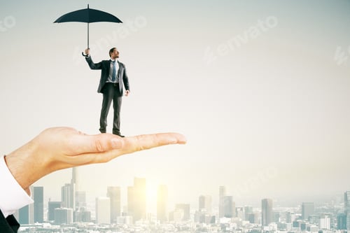 Preview: Big Hand Holding Young Businessman With Umbrella On Bright City Background With Sunlight