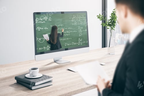 Preview: European Businessman At Office Desk Looking At Computer Screen With Online Education Chalkboard And