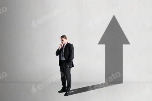 Preview: Businessman With A Shadow In The Shape Of An Arrow Up On The Blank White Concrete Wall Background