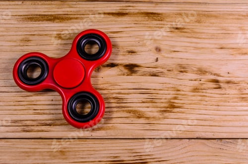 Preview: Red Fidget Spinner On Rustic Wooden Desk. Top View