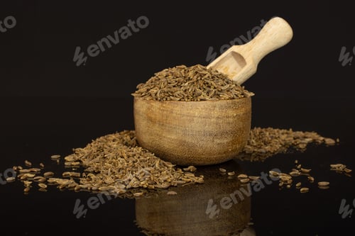 Preview: Lot Of Whole Dry Caraway Fruits In A Wooden Bowl With Wooden Scoop Isolated On Black Glass