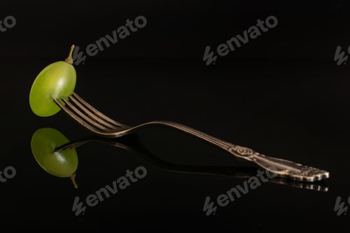 Preview: One Whole Fresh Green Grape With Antique Fork Isolated On Black Glass