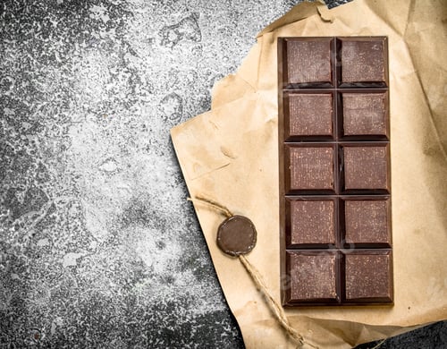 Preview: Chocolate Bar In A Paper Wrapper. On A Rustic Background.