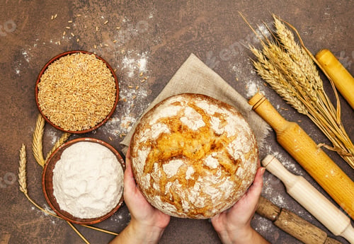 Preview: Female Hands Hold Freshly Baked Bread. Wheat Ears, Wooden Rolling Pins And A Bowls Of Flour And