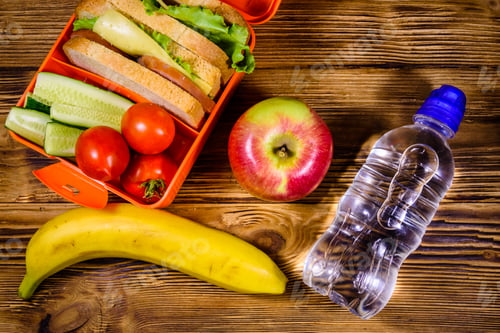 Preview: Ripe Apple, Banana, Bottle Of Water And Lunch Box With Sandwiches, Cucumbers And Tomatoes On Rustic