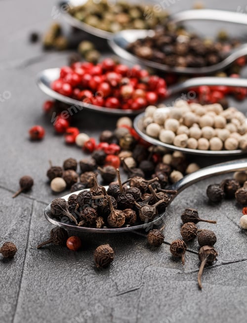 Preview: Colorful Peppers In Spoon On Black Table - Cubeb, Pink, Green And White Closeup. Spices. Selective