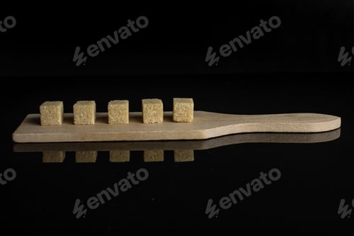 Preview: Group Of Five Whole Sweet Brown Sugar Cube On Small Wooden Cutting Board Isolated On Black Glass